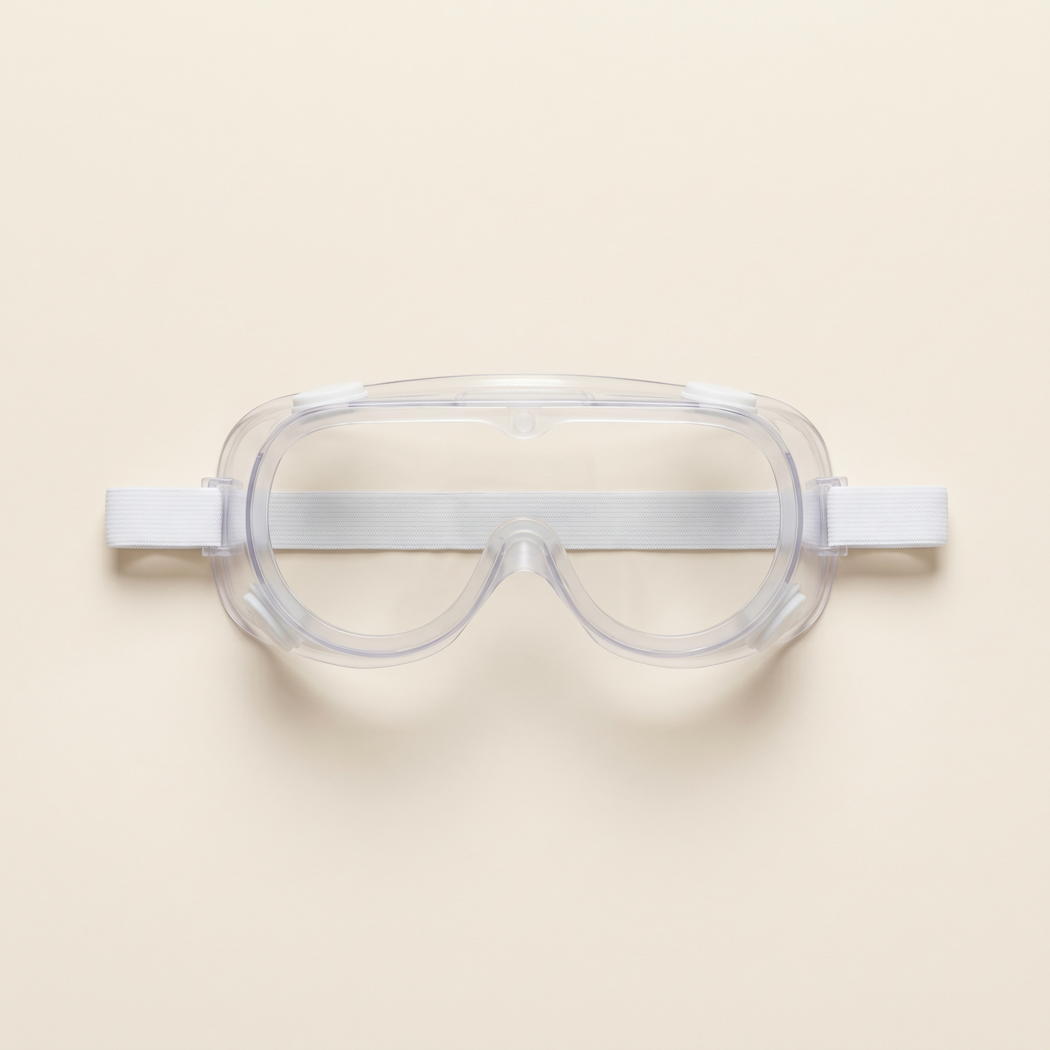 Skyddsglasögon — transparenta plastlinser med svart mjukt sidoskydd, ligger på cremefärgad bakgrund.
